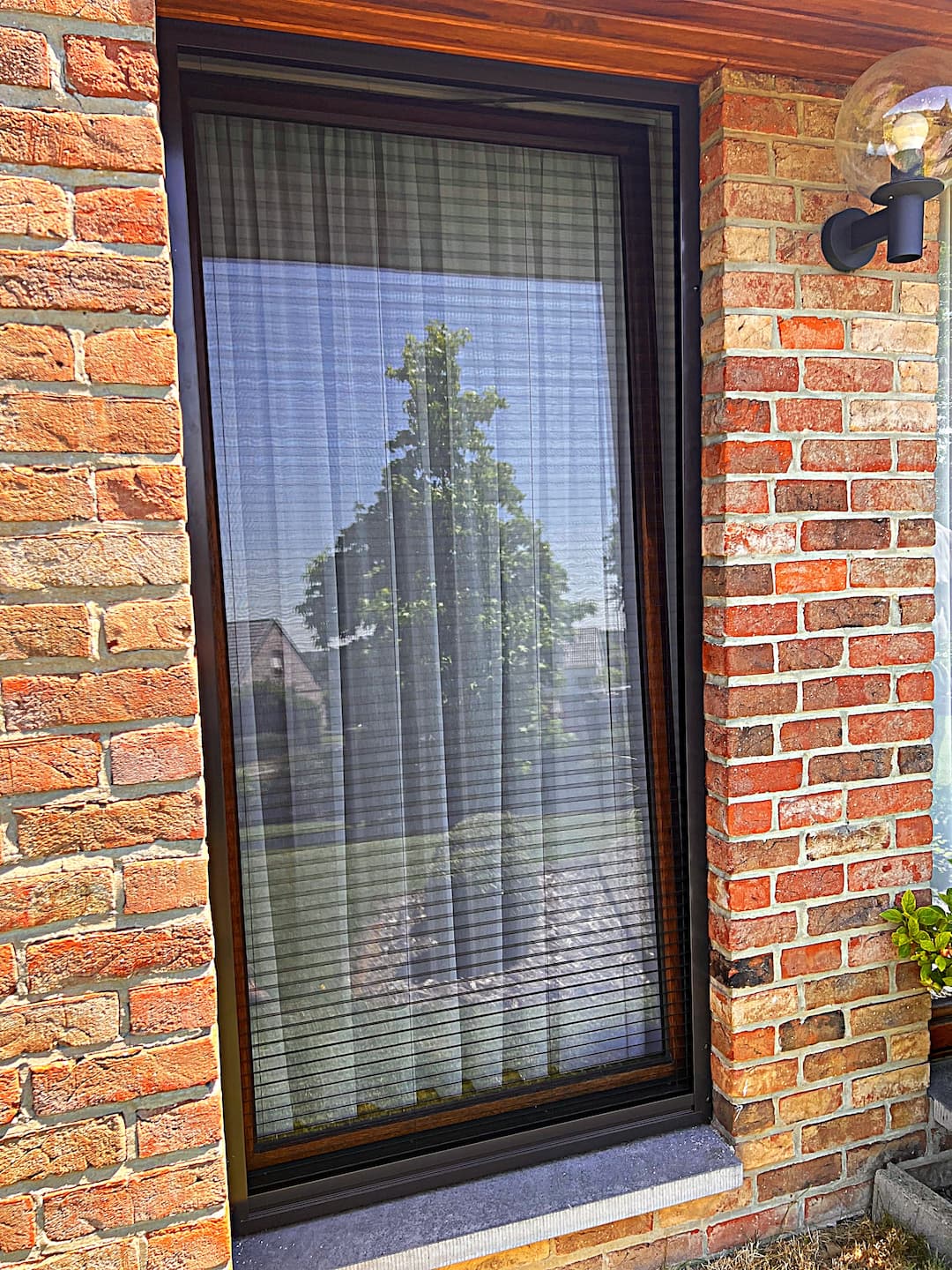 Moustiquaire fice sur fenêtre en bois, cadre noir, façade en brique rouge