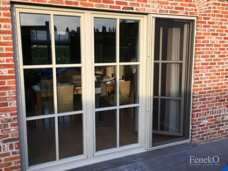 Porte moustiquaire battante sur porte fenêtre à cadre blanc , mur en brique rouge