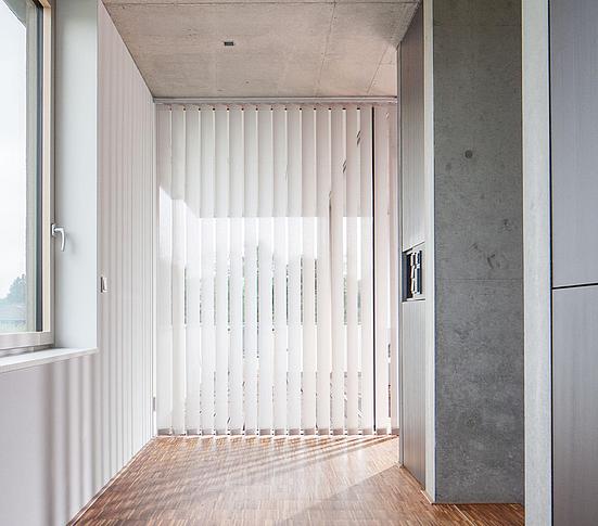 Store lamelle blanc au fond, parquet et murs en béton